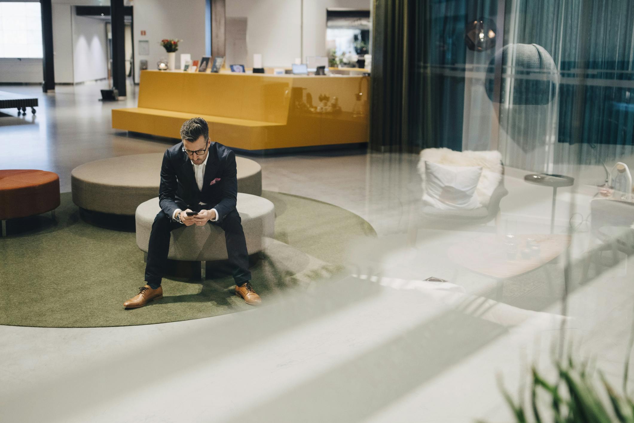 Full length of businessman using mobile phone while sitting in lobby at office